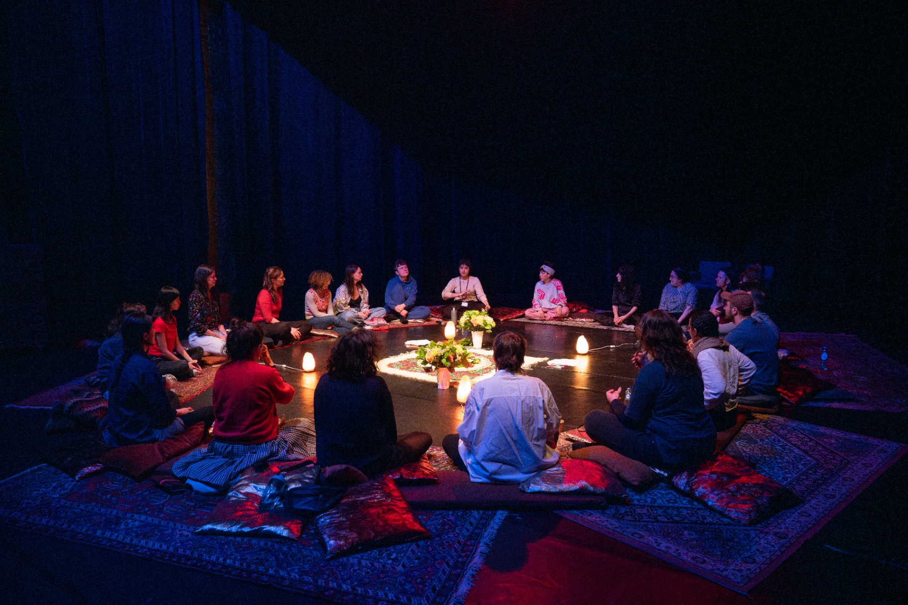 Participants seated in a circle of candlelight and rugs for The Circle of Grieving Voices