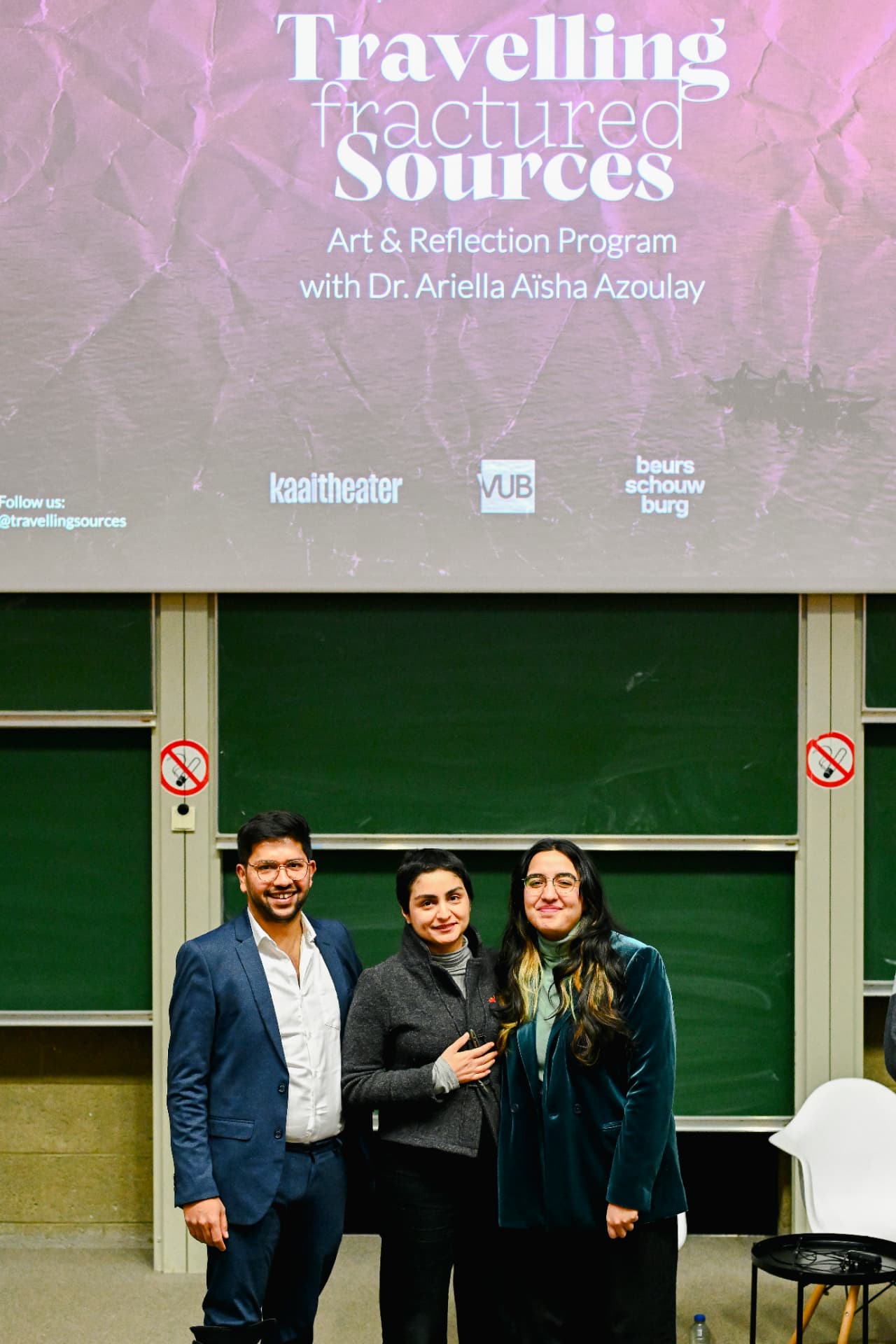 Three speakers posed in front of a green chalkboard at Travelling Fractured Sources