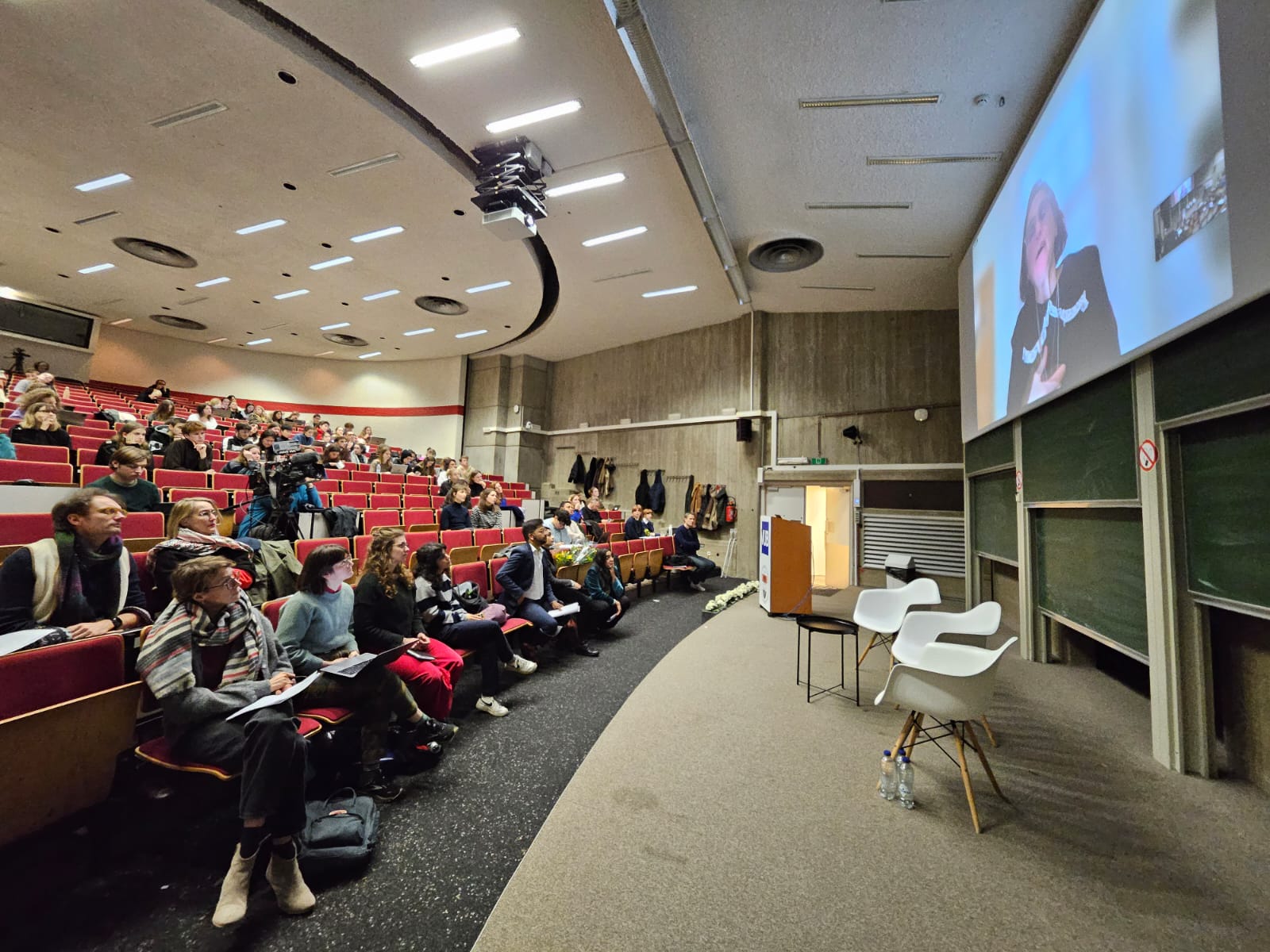 Lecture hall with tiered seating and a projected speaker close-up