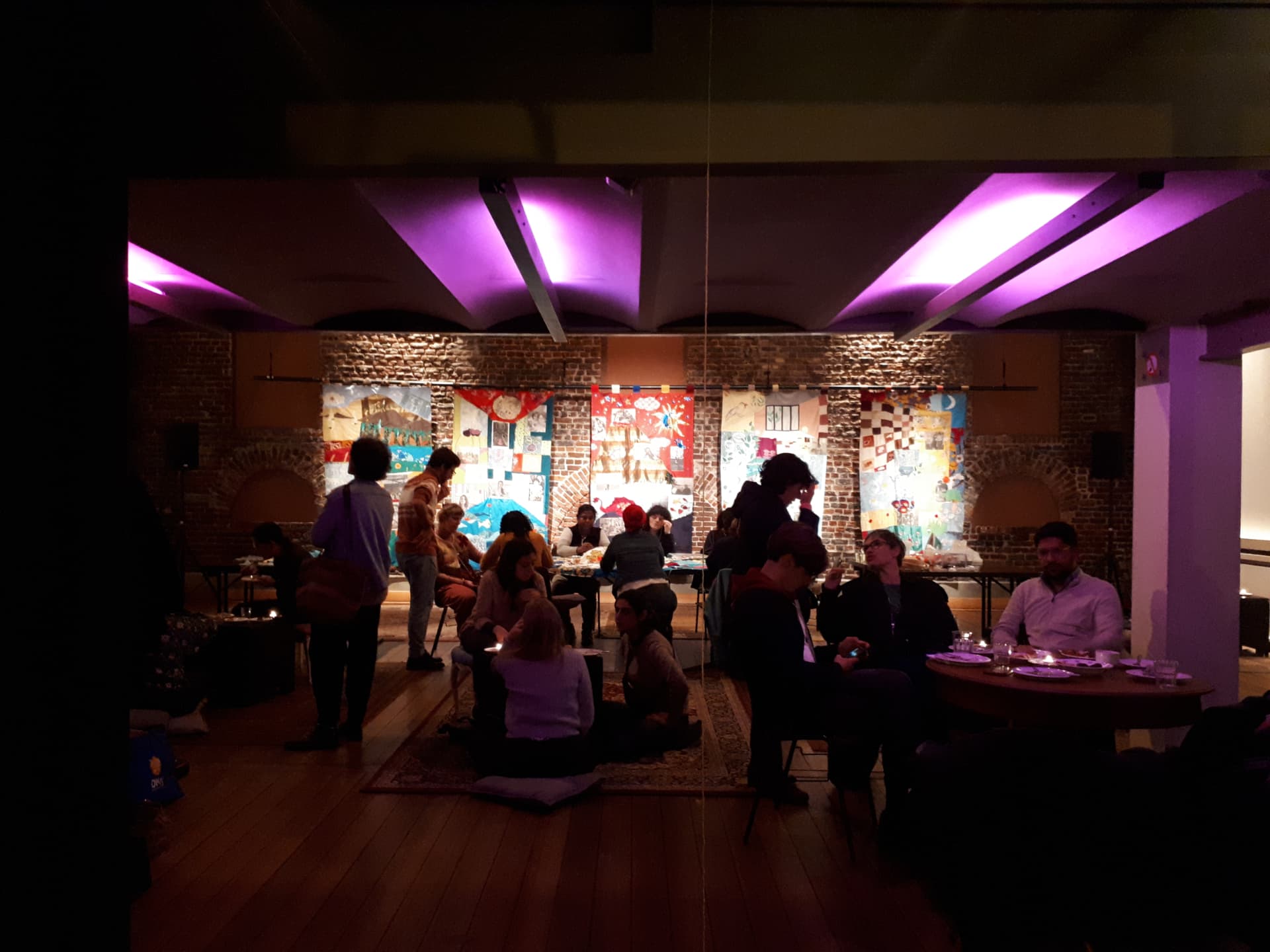 Indoor gathering with banners and purple lighting at Travelling Sources
