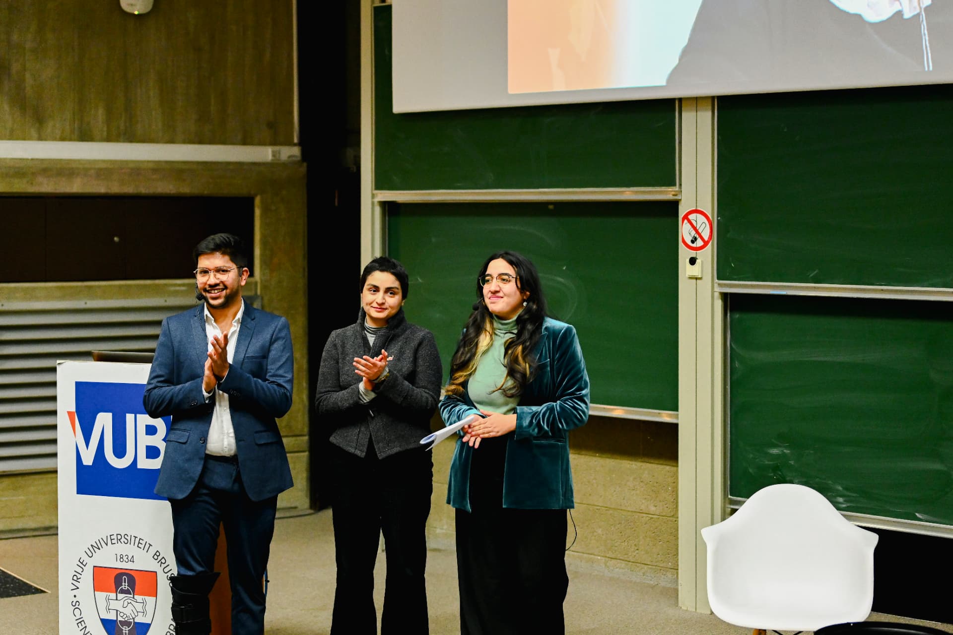 Three speakers applauding on stage next to a VUB podium